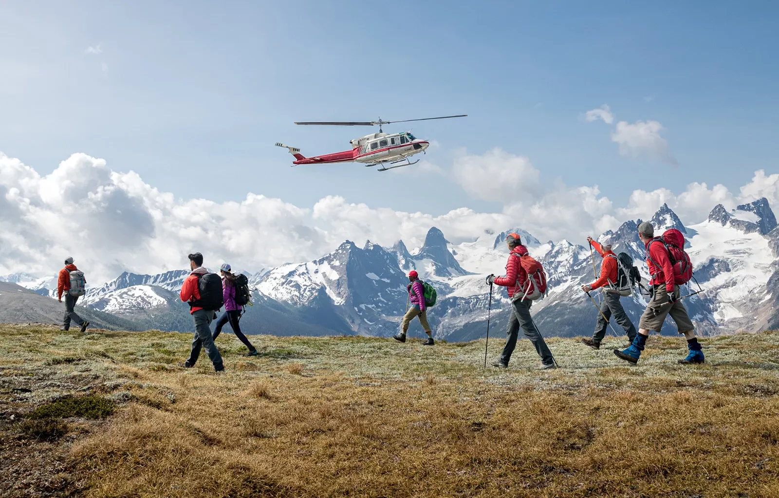 Group of guests beginning mountain hike , waving goodbye to helicopter.