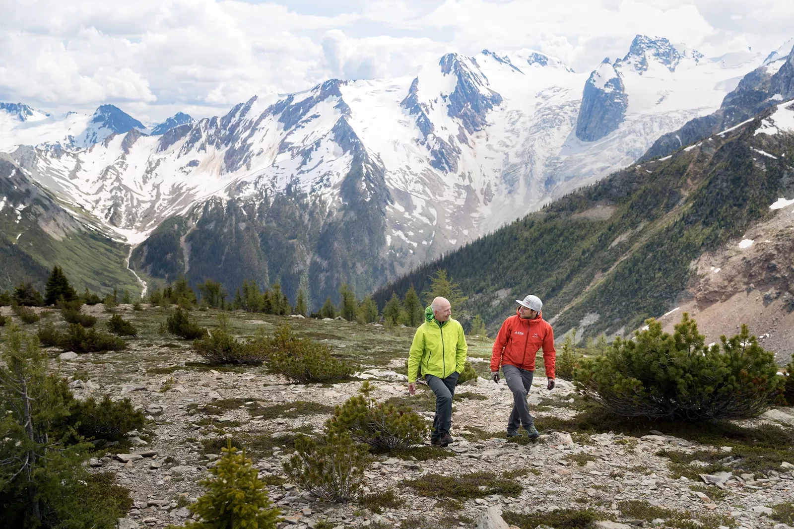 Two guests walking on hillside, Bugaboos in background.