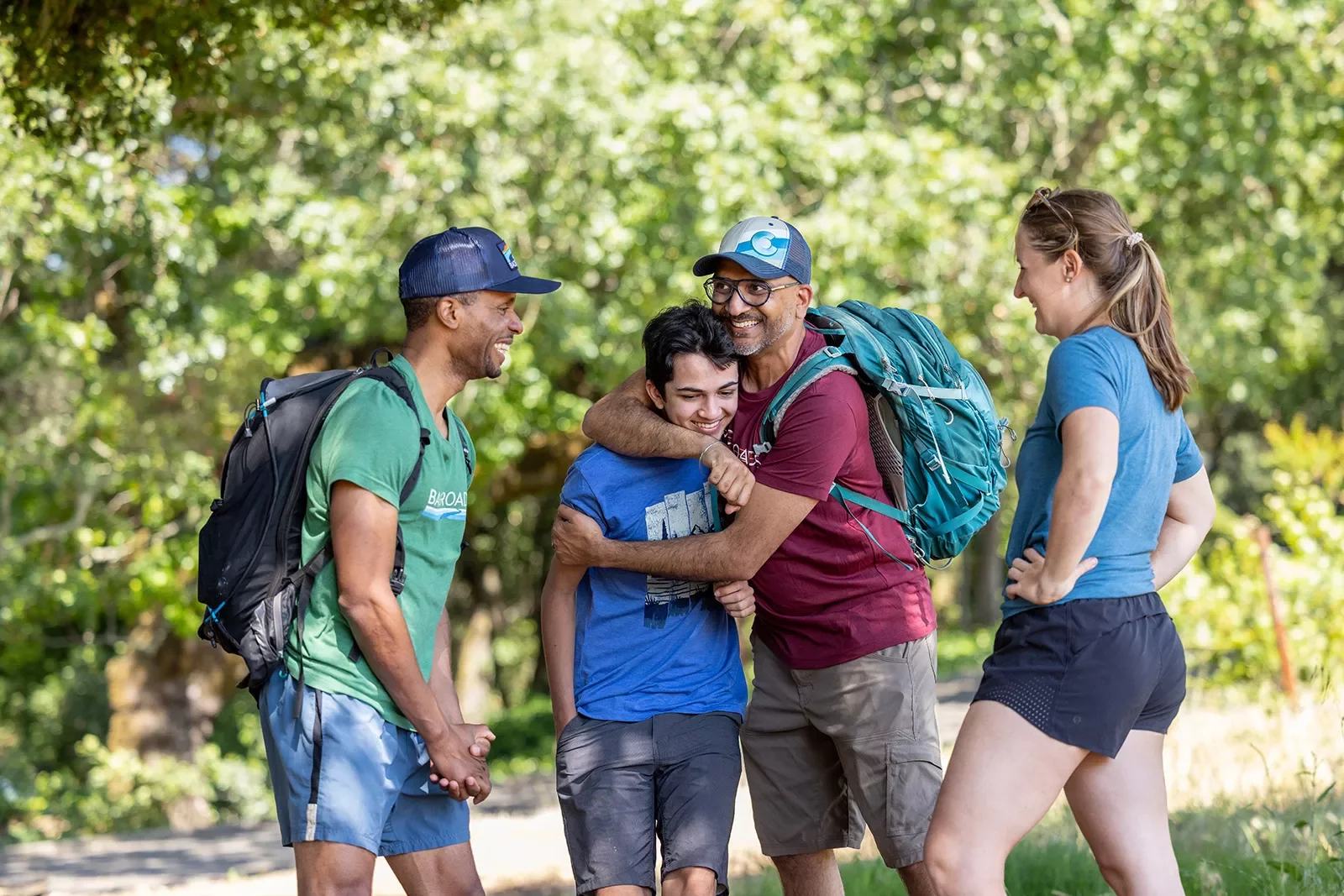 Four guests on the trail, smiling at each other, one is hugging another.