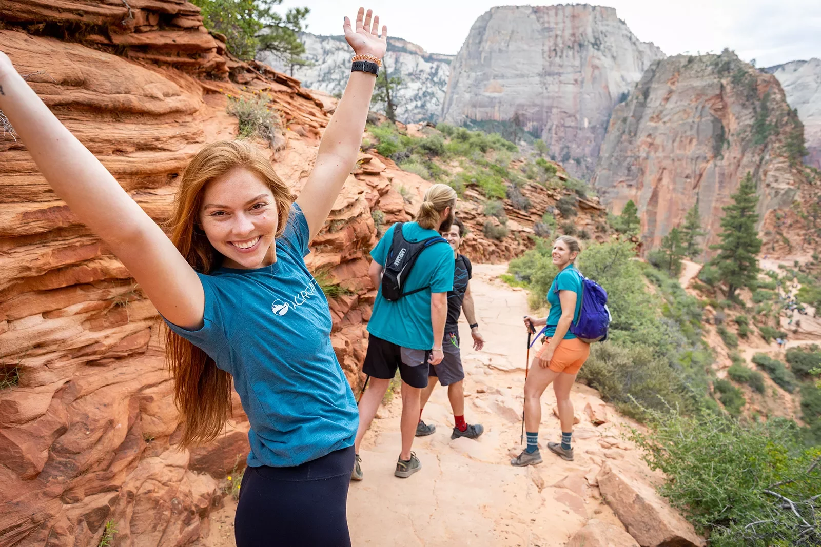 Redhead model with arms up behind guests in Zion