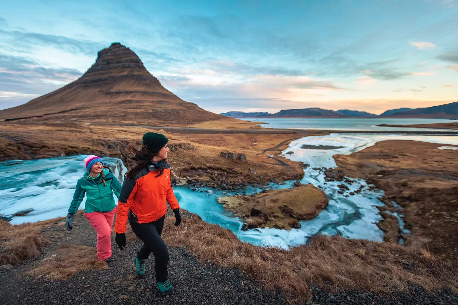 Two hikers walking along side stream of water in Iceland.