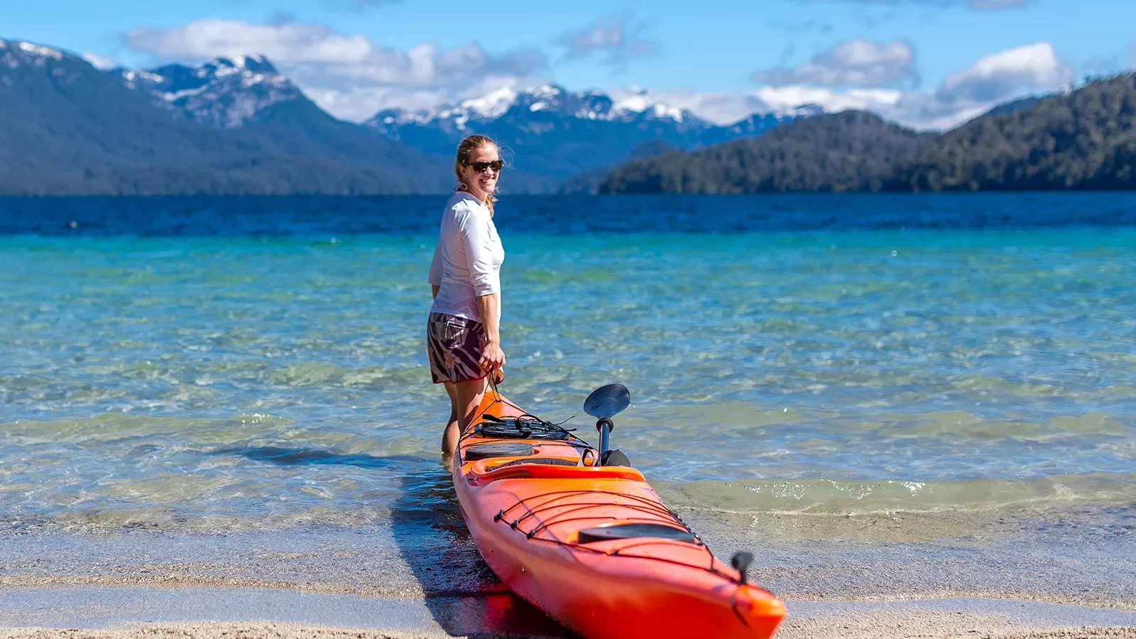 Guest pulling their kayak out to sea, large mountain range behind her.