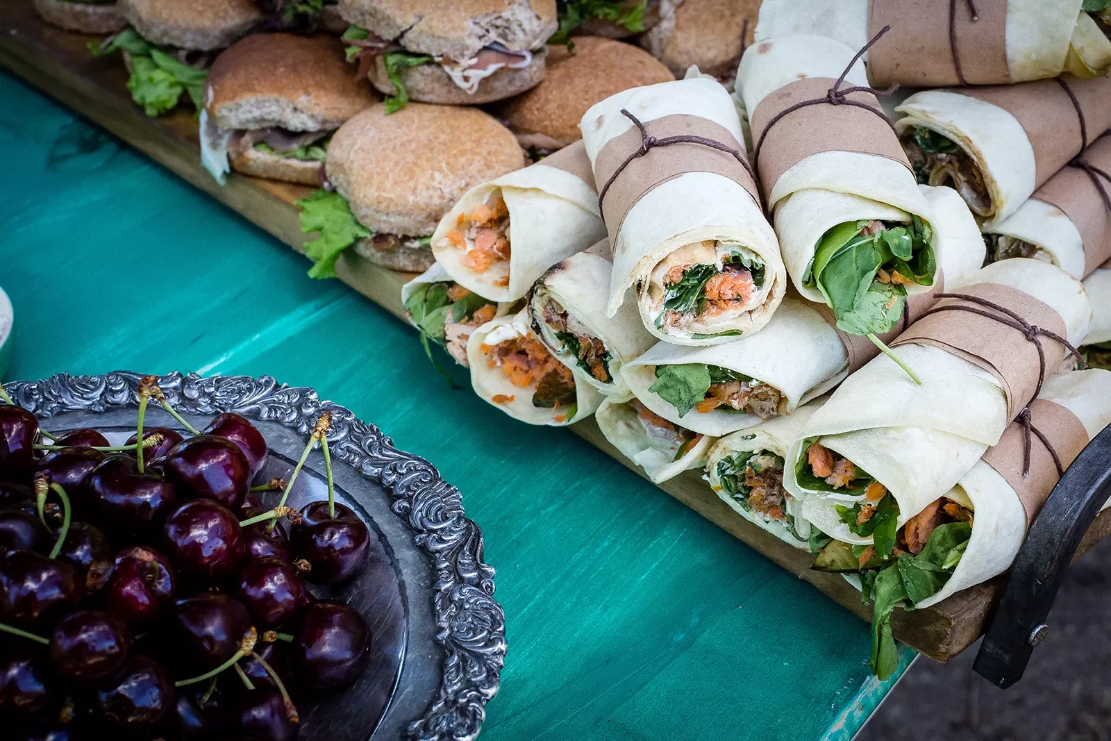 Platter of sandwiches and wraps, cherries.