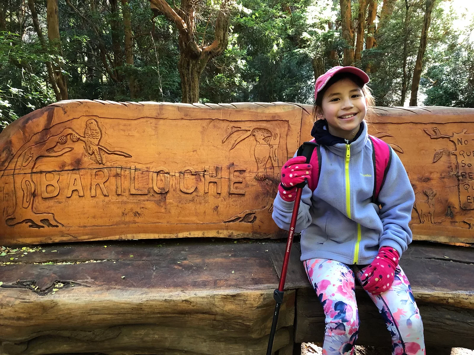 Young guest sitting on carved bench, &quot;BARILOCHE&quot; inscribed behind her.