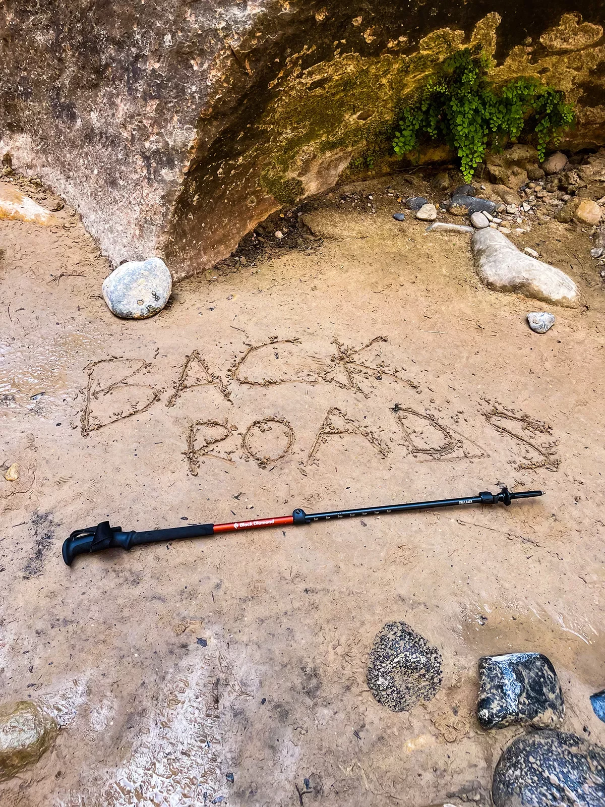 Shot of hiking pole on trail, &quot;Backroads&quot; etched into the mud above.