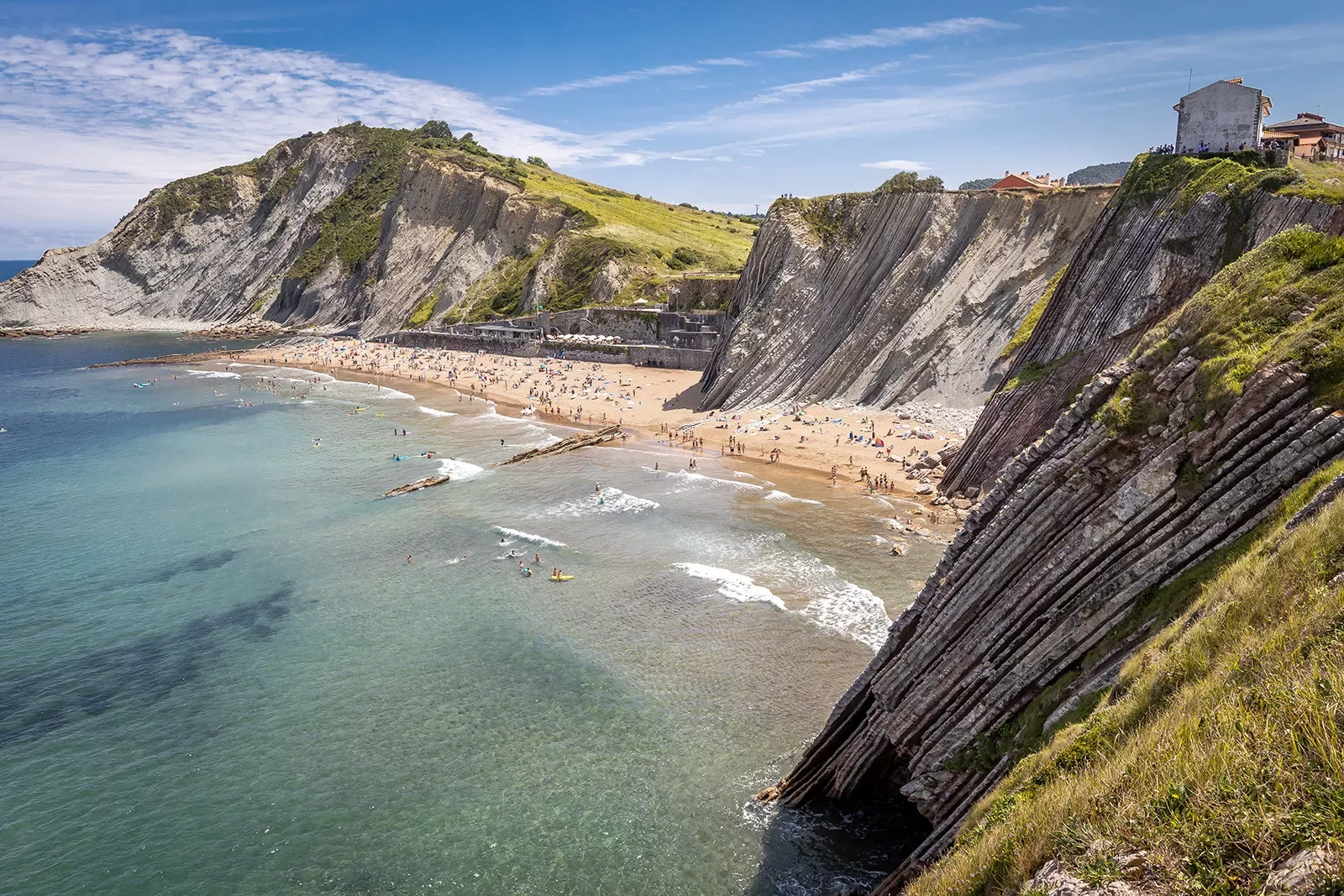Shot of craggy cliffs, large, crowded beach in distance.