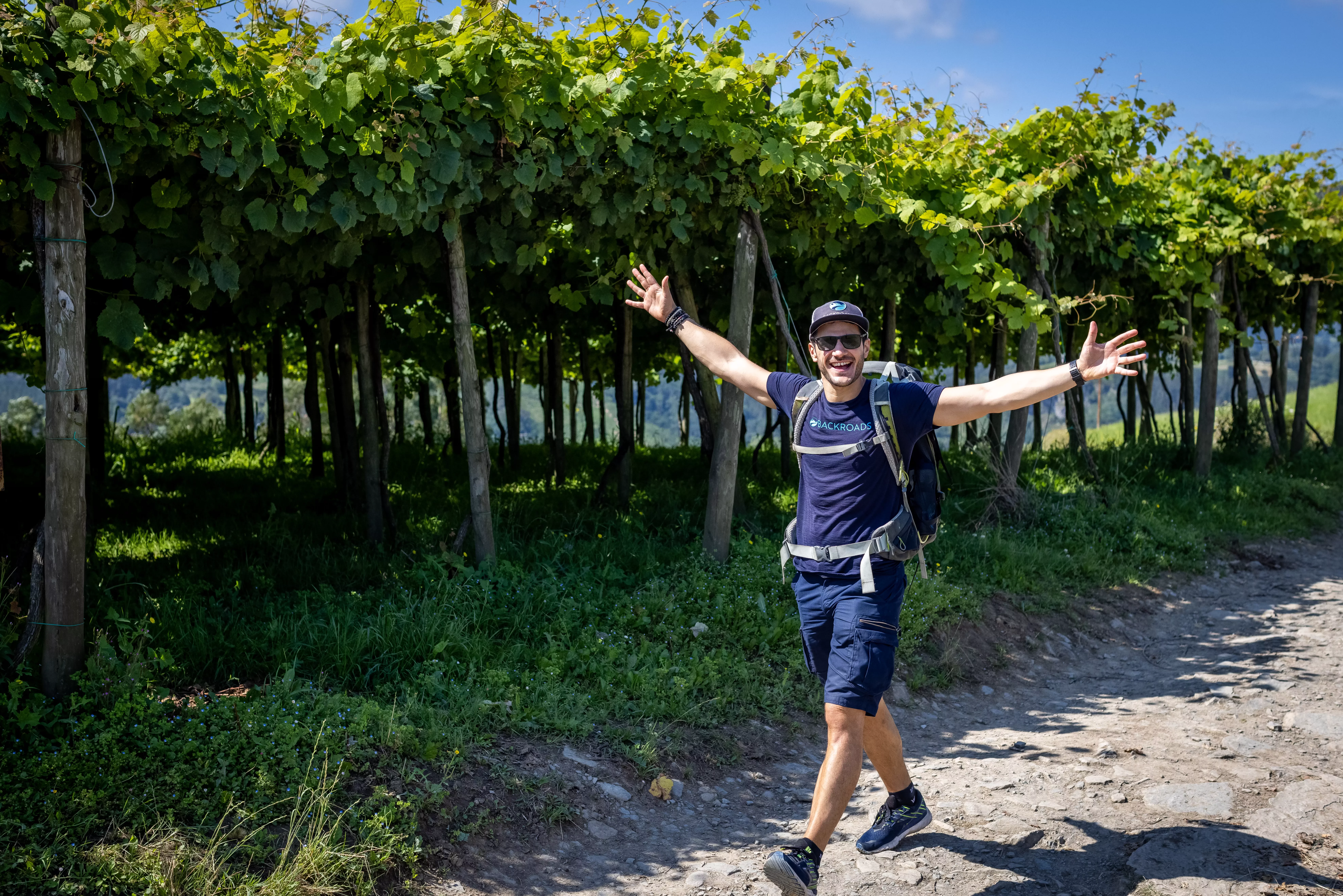 Leader walking past tall grapevines, arms outstretched.