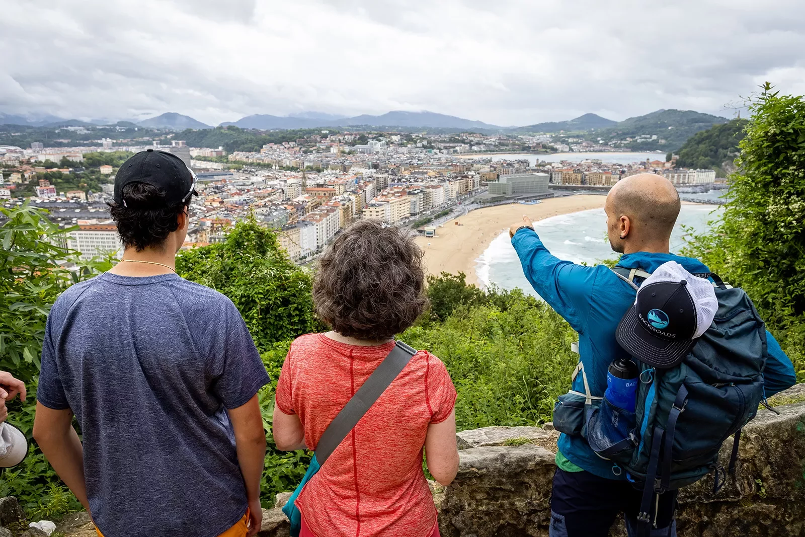 Two guests &amp; leader overlooking French coastal town, leader pointing to something.