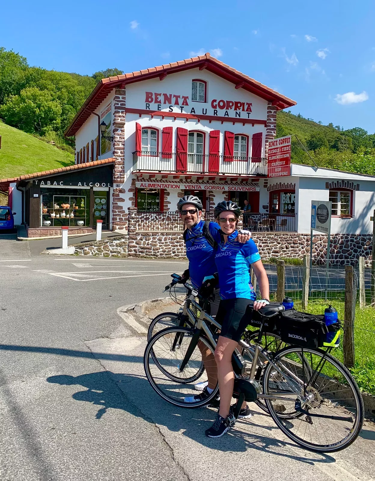 Two guests on bikes in front of &quot;Benta Gorria&quot;, a red and white building.