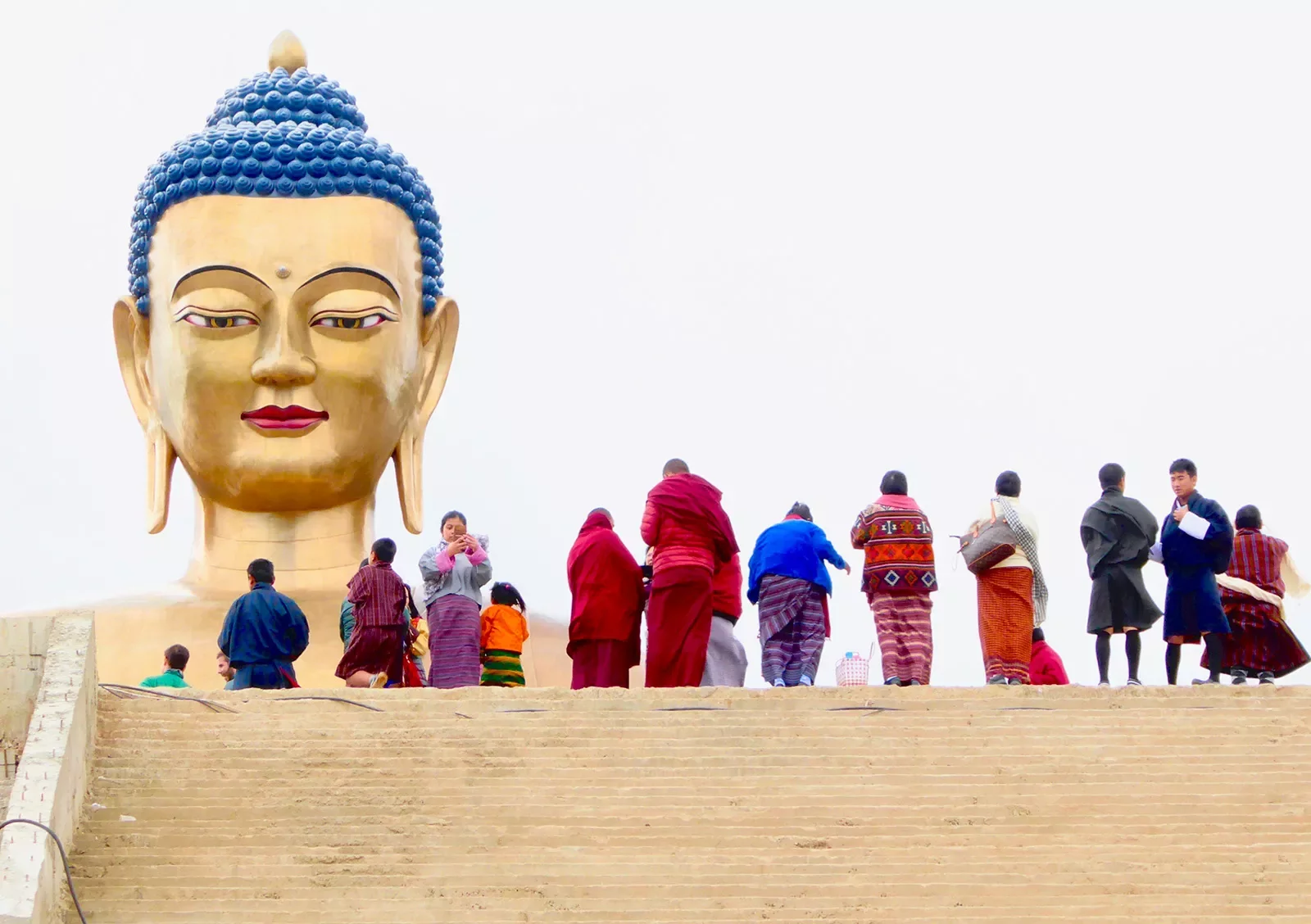 Group of travelers at the top of a large staircase standing before a large, gold Buddha head