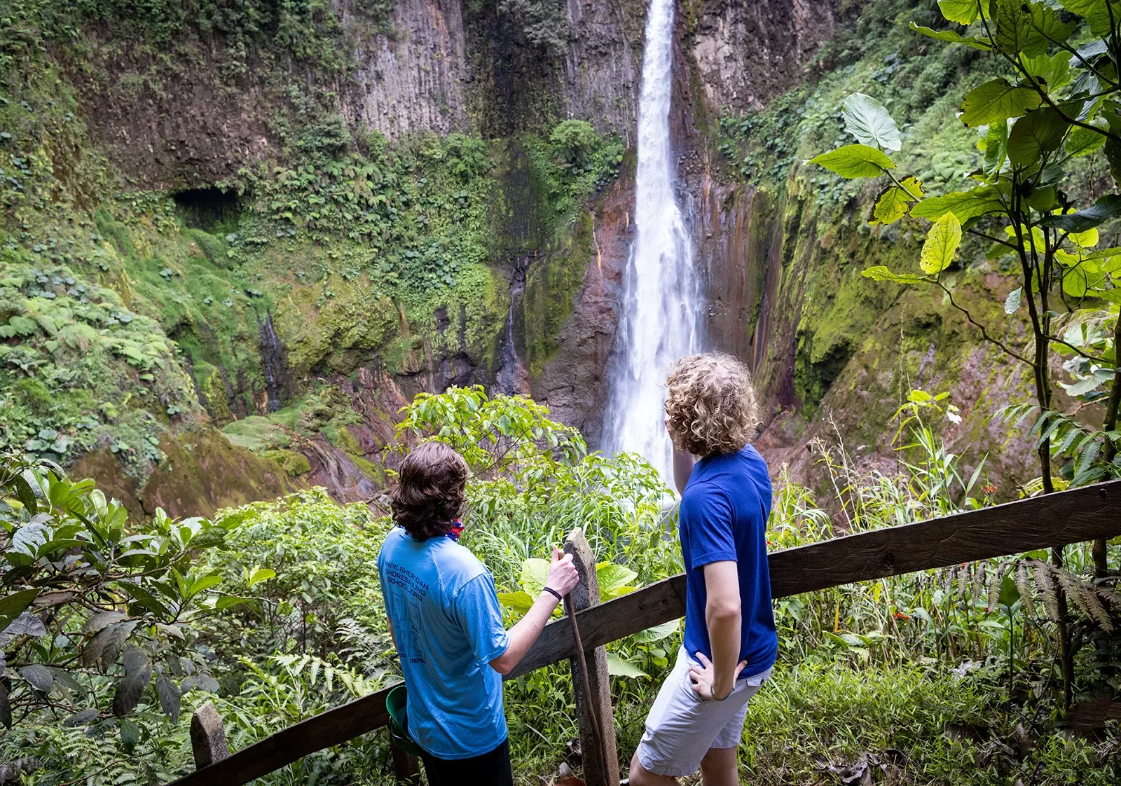 Two guests on forest path, looking down at forest, waterfall.