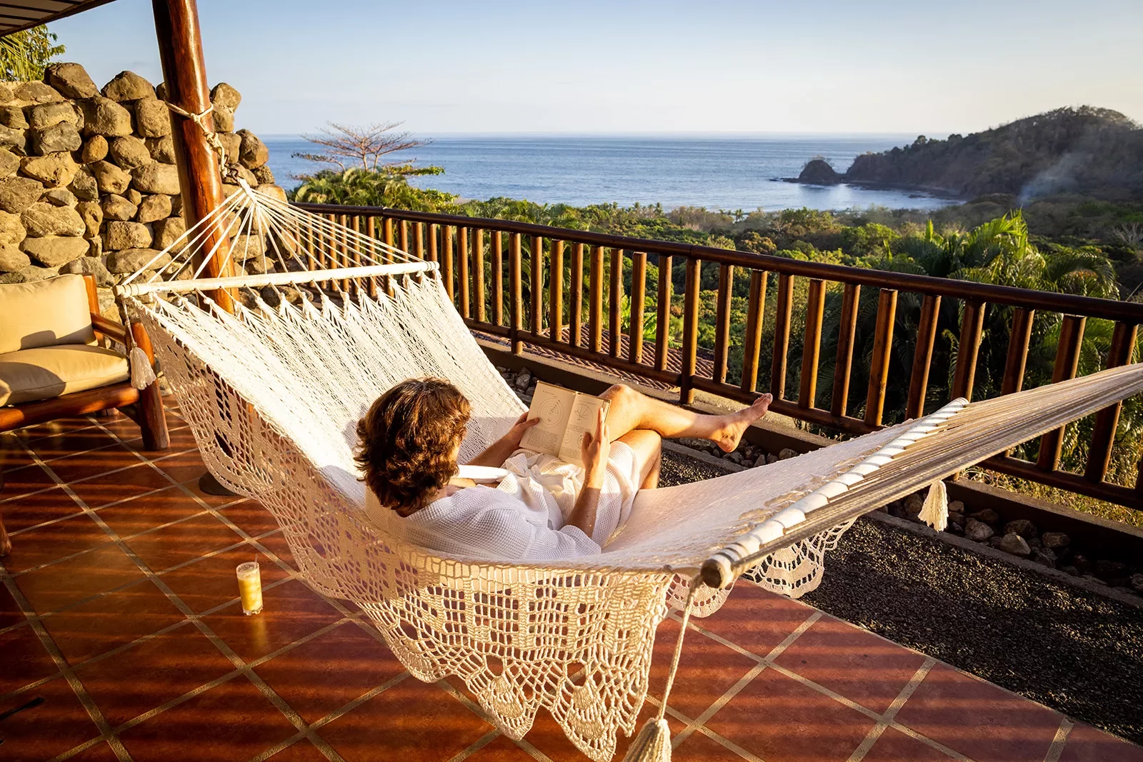Guest on hotel balcony, hammock, overlooking forest, ocean.