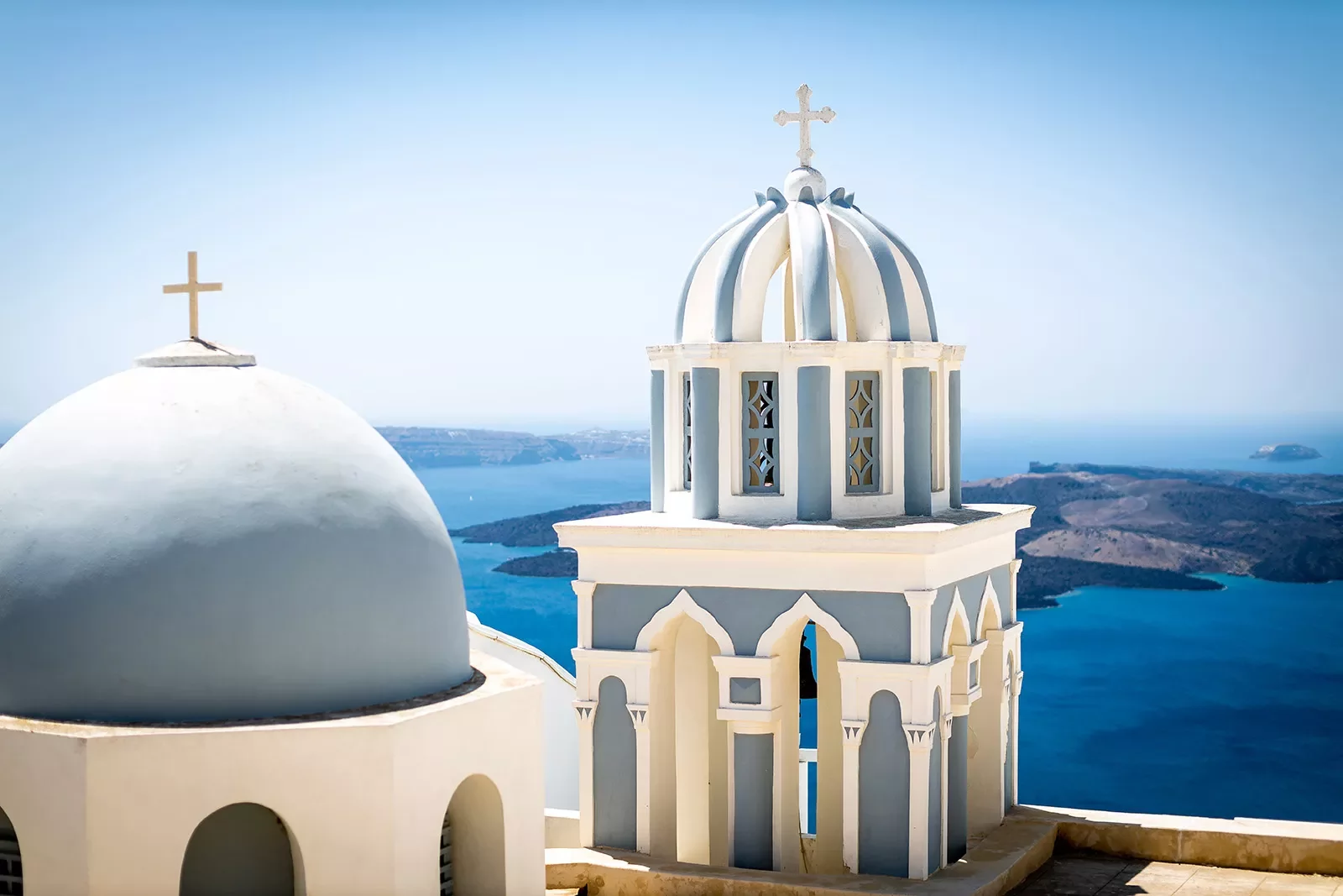 Close up of blue domes of Santorini, ocean behind them.