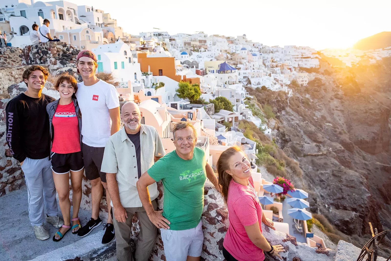 Group of guests among cliffside, whit houses, sunset behind them.