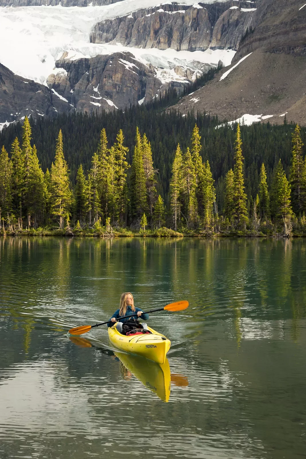 Guest kayaking in lake, forest, hills in distance.