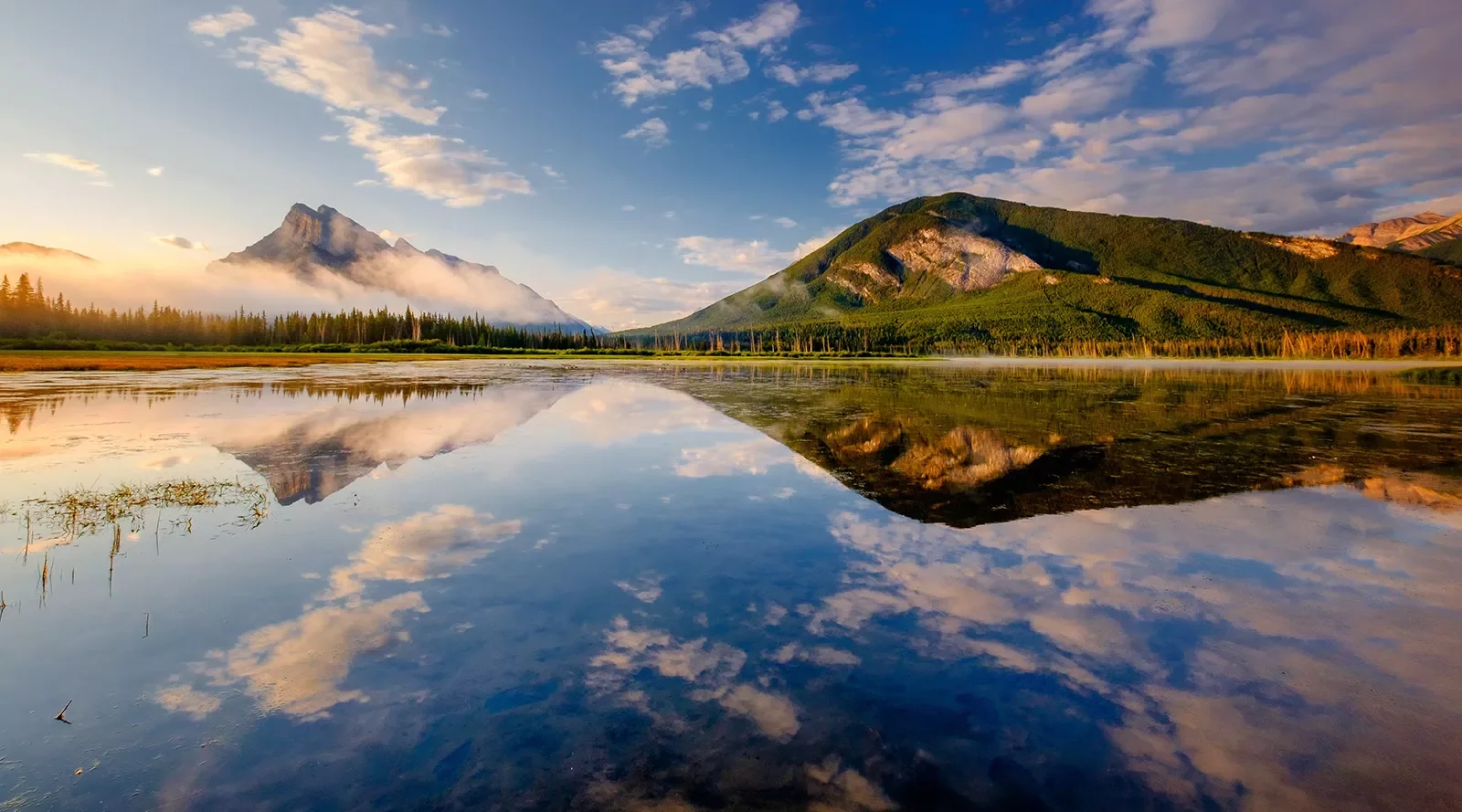 Wide shot of reflective lake, mountains during sunset.