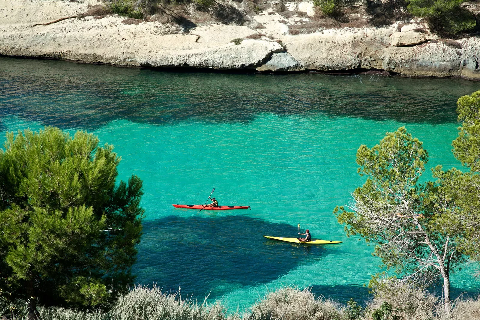 Wide shot of two guests kayaking through blue water.