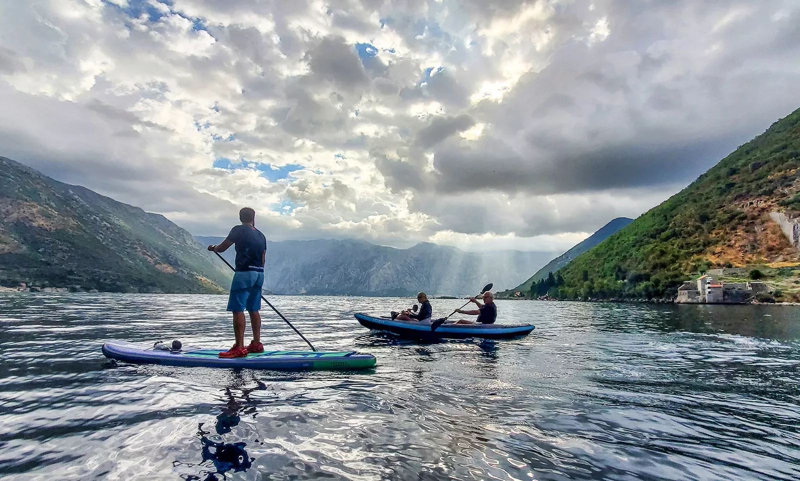 Two guests kayaking, one paddle boarding, clouds, hills in distance.