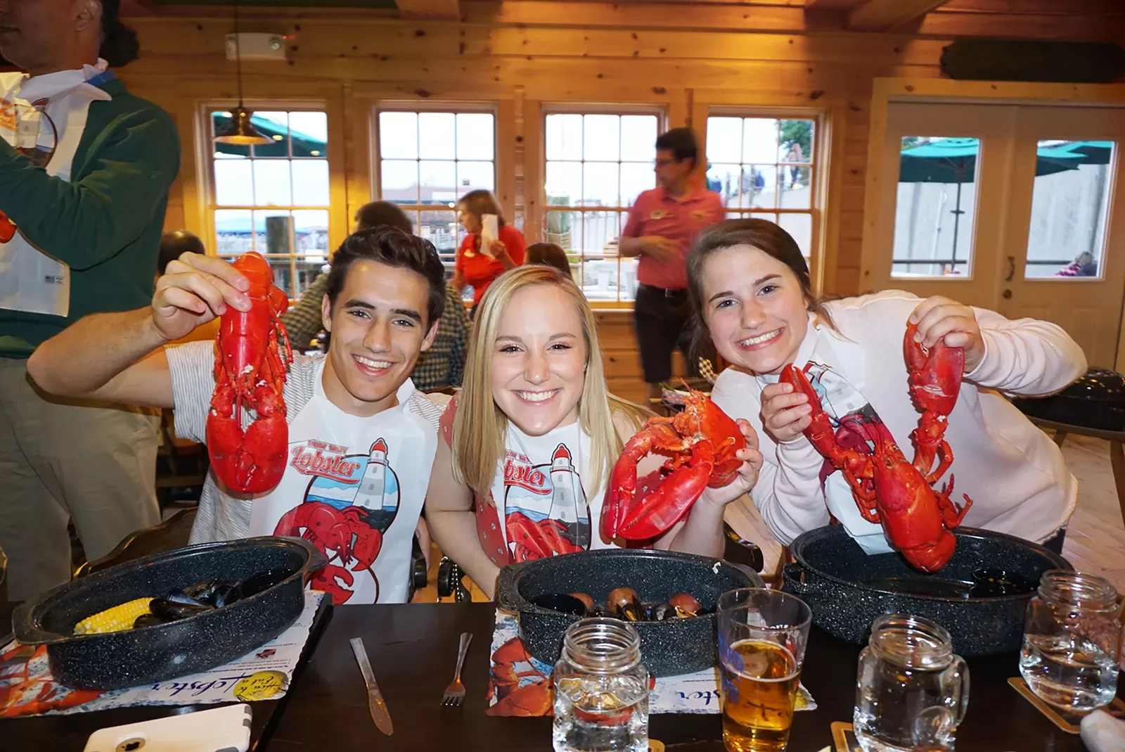 Three young guests holding up cooked lobsters during a meal.