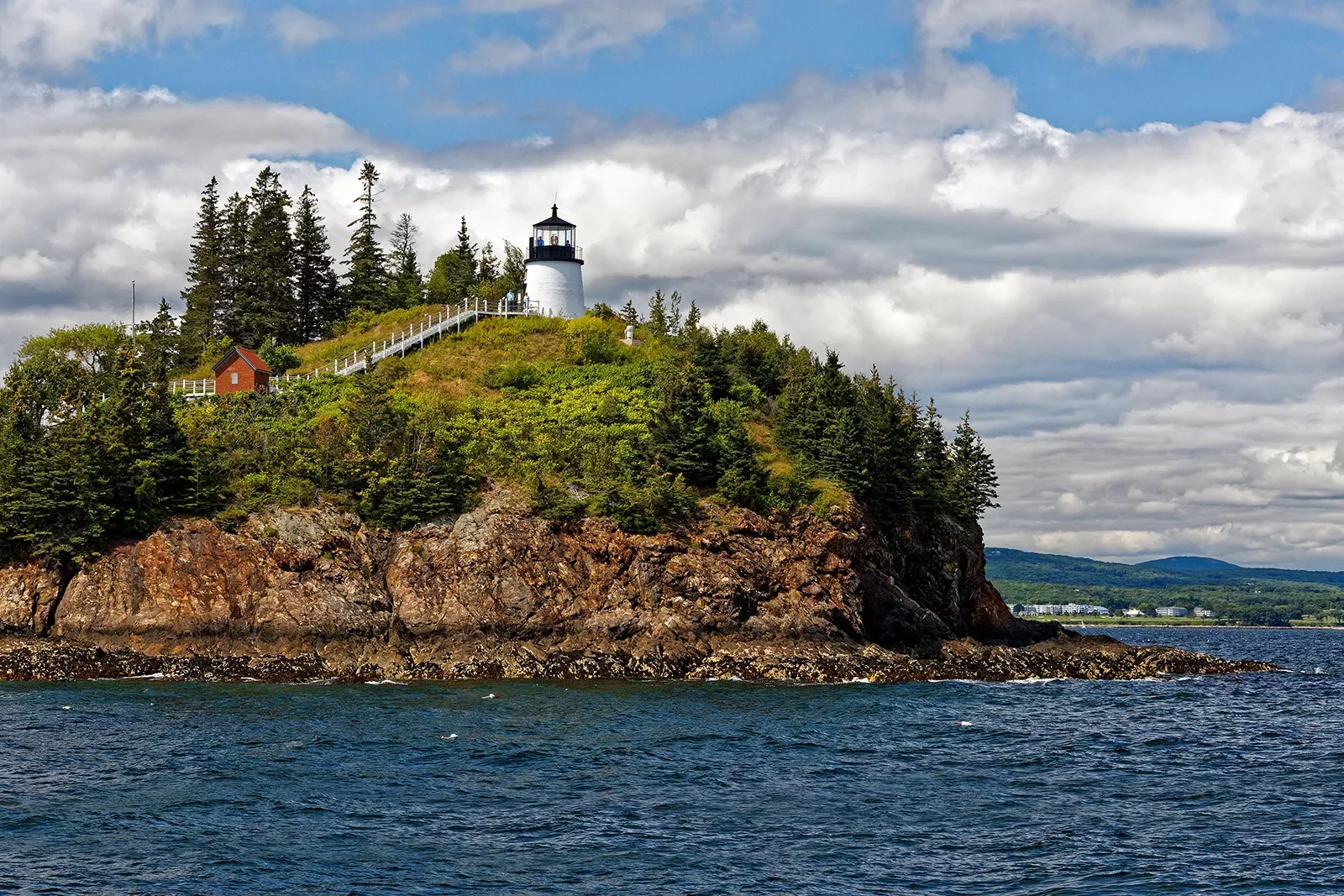 Wide shot of small island, white lighthouse and small red building on it.
