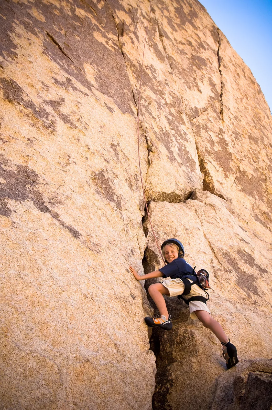 Child rock climbing on sandy cliffside.