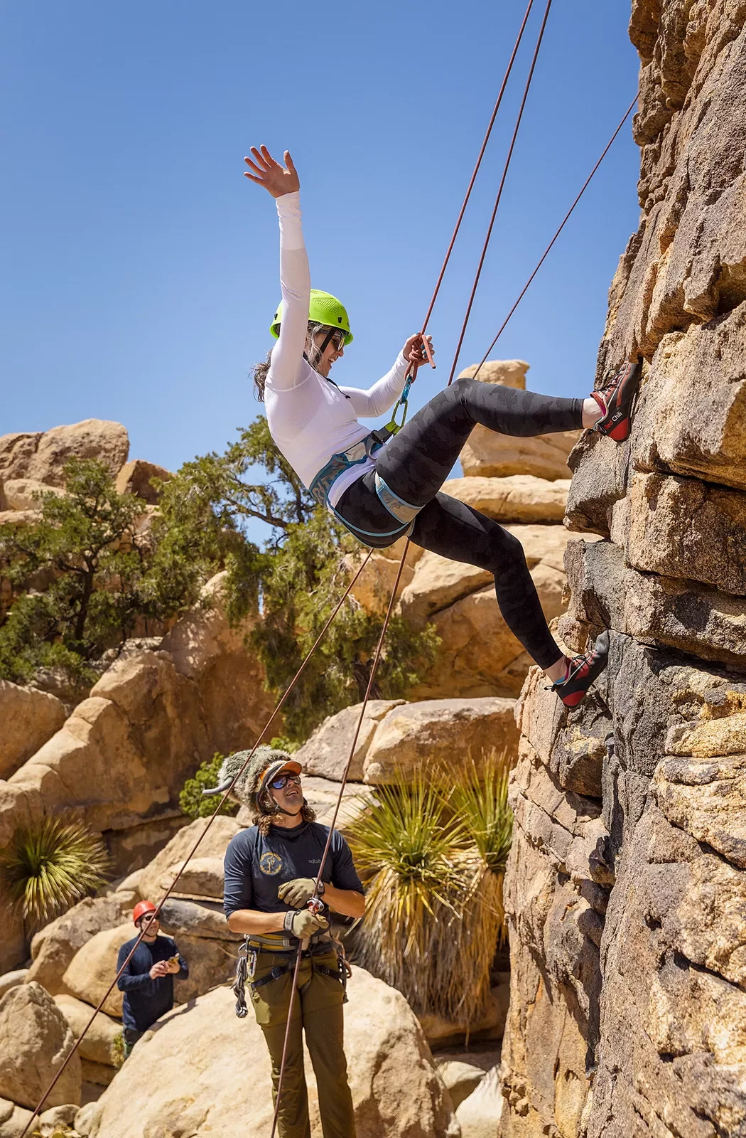 Three guests rock climbing, one is waving to the camera.