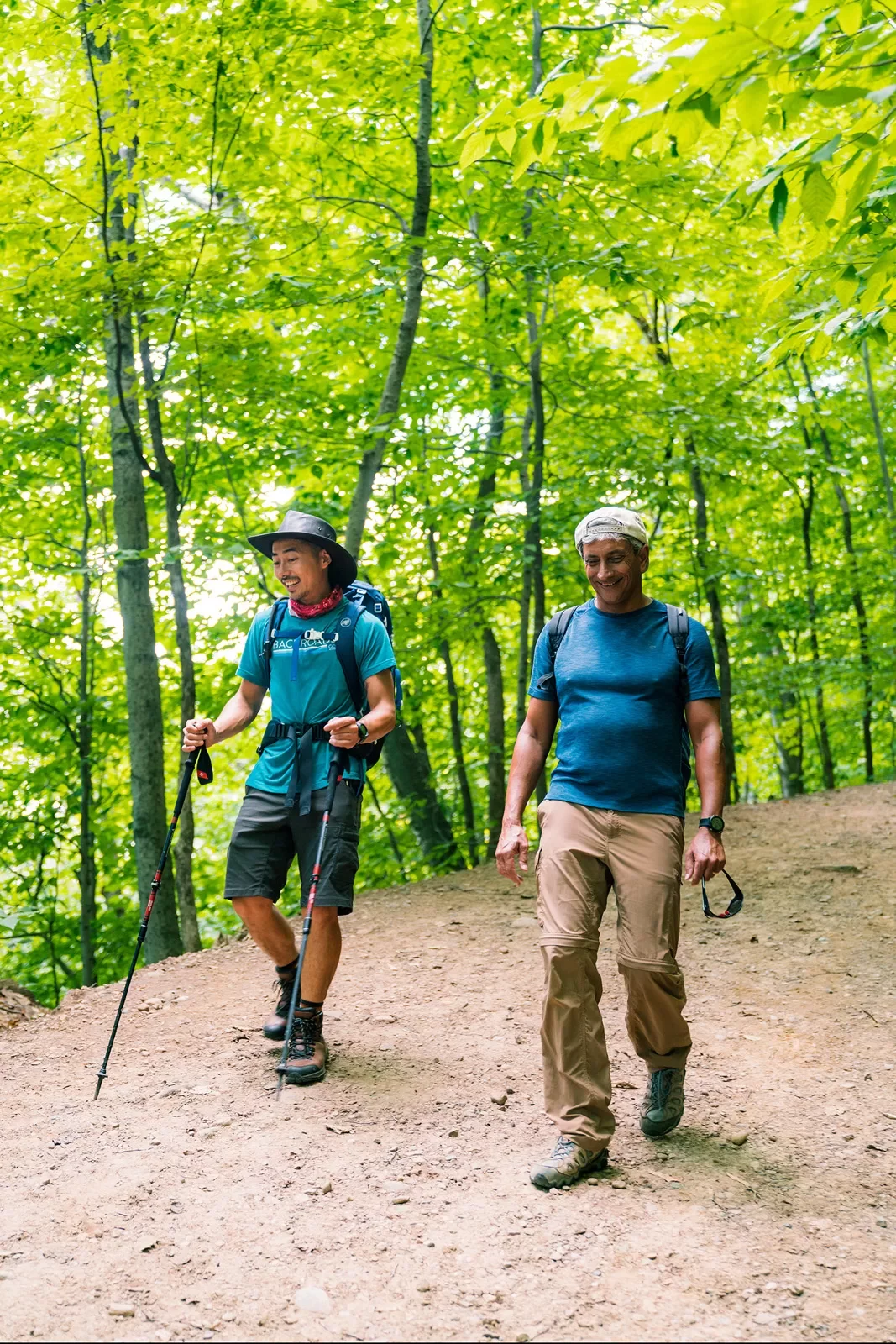 Two guests with hiking gear walking down forest trail.