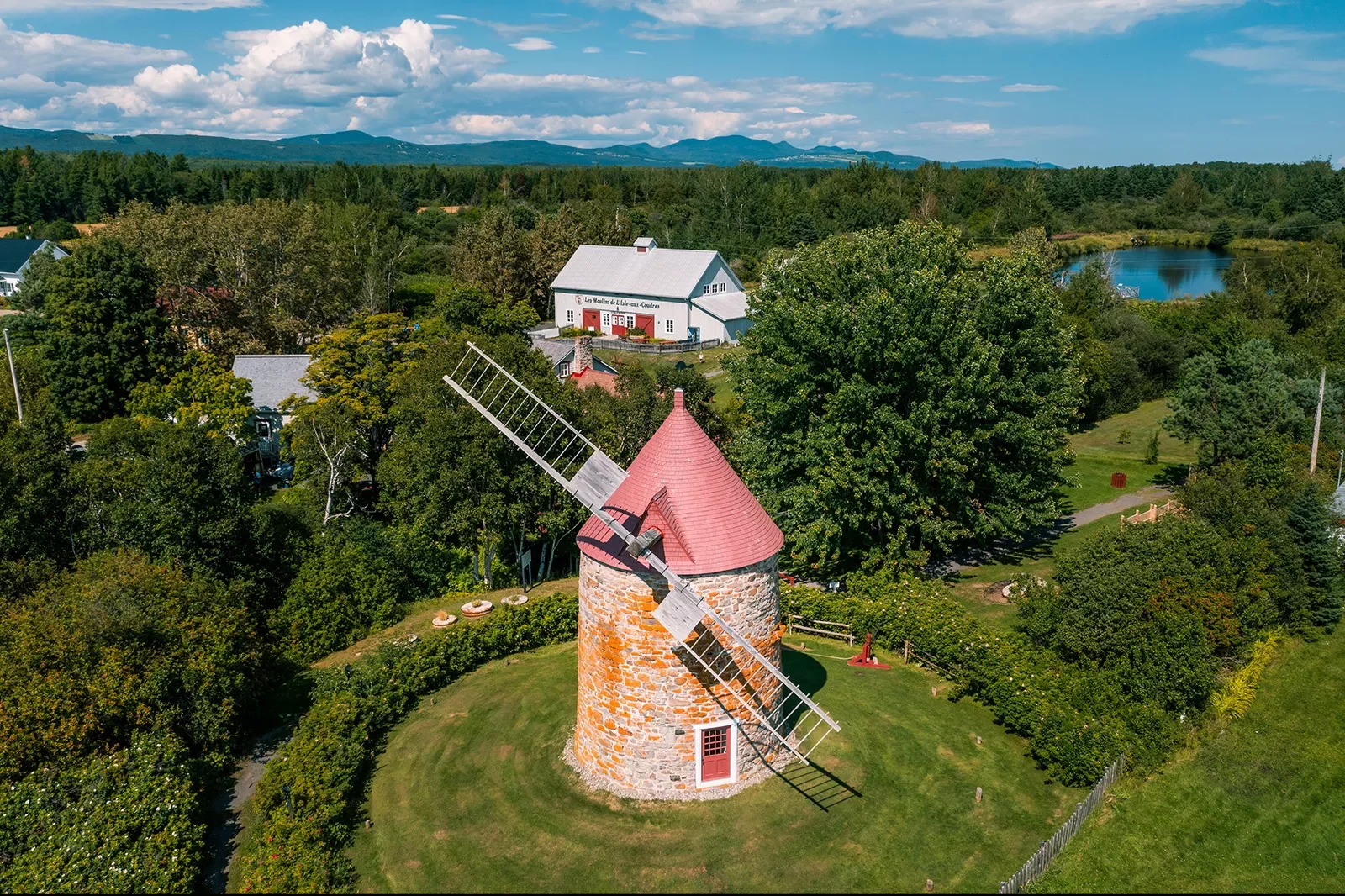 Wide shot of large windmill, white building in background.