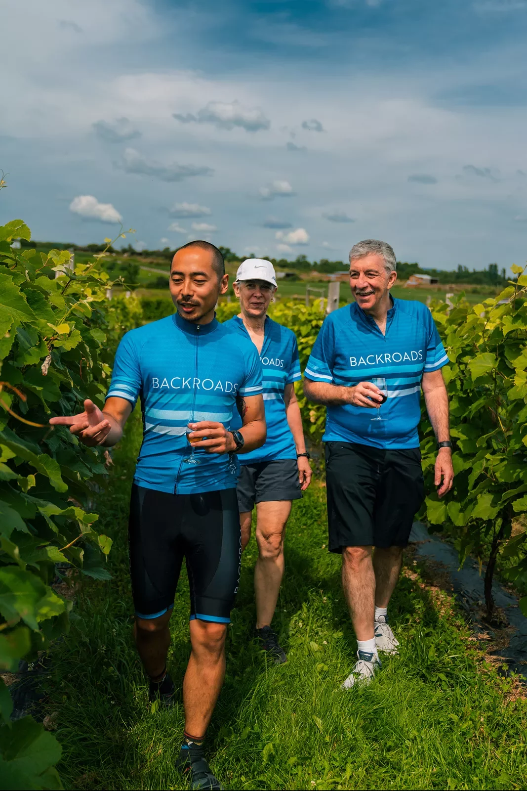 Three guests walking through vineyard, one pointing to grapes.