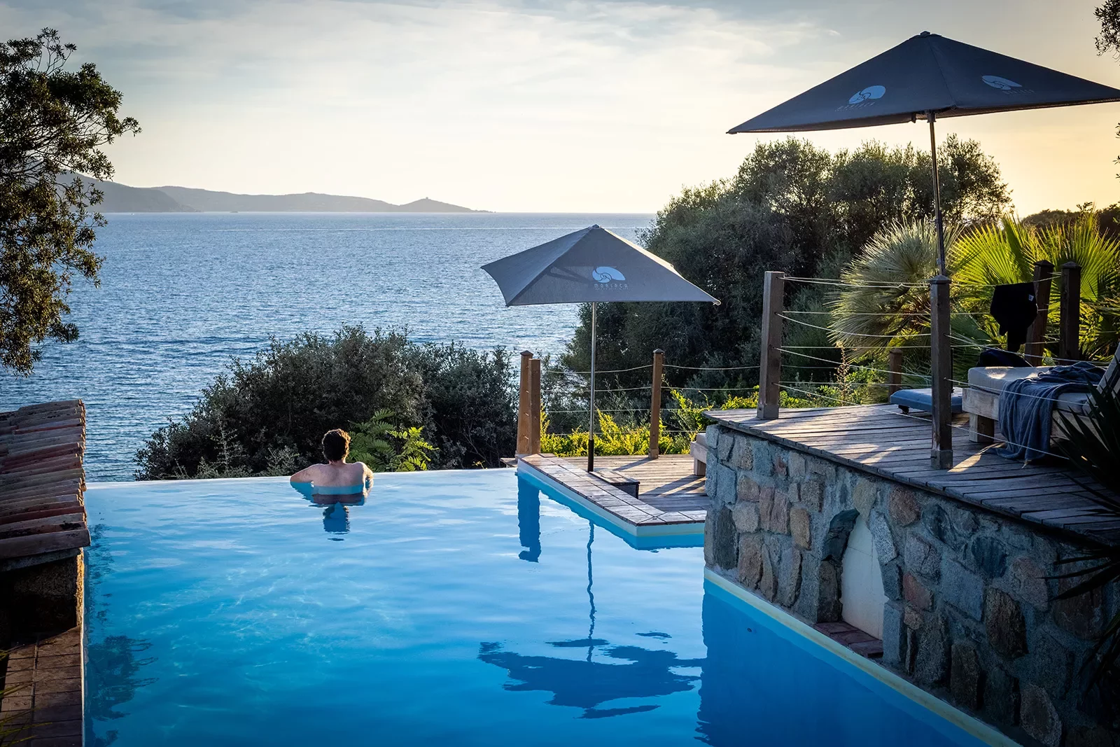 Guest relaxing in a pool, overlooking ocean and distant hills.