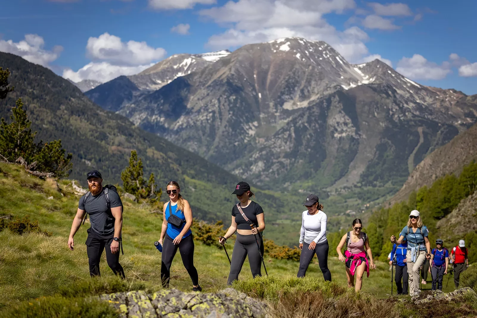 Group of young hikers climbing a grassy hill with large mountains in the background