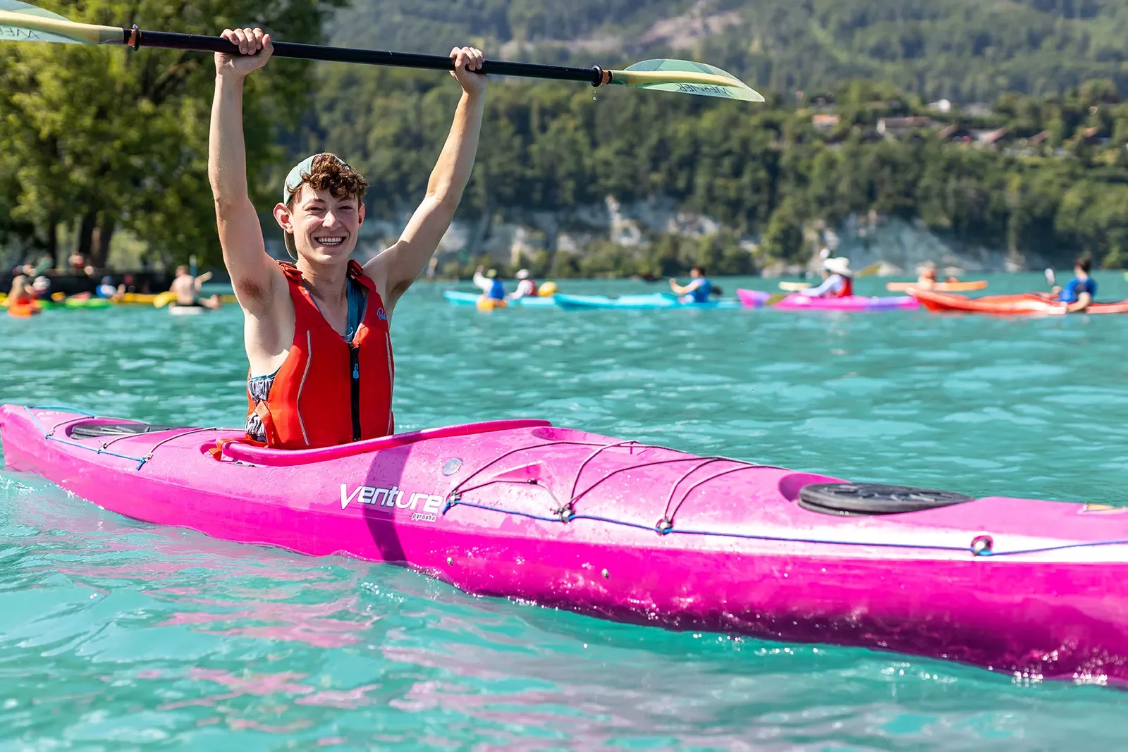 Young man sitting in pink kayak holding his oar overhead
