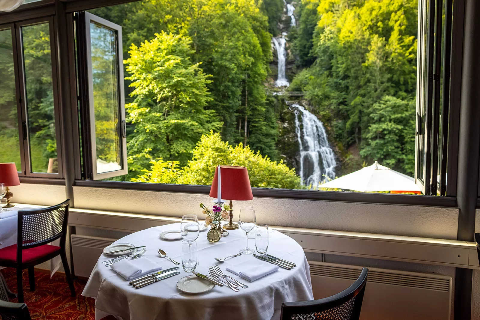 Shot of dining room, waterfall, forest out window.