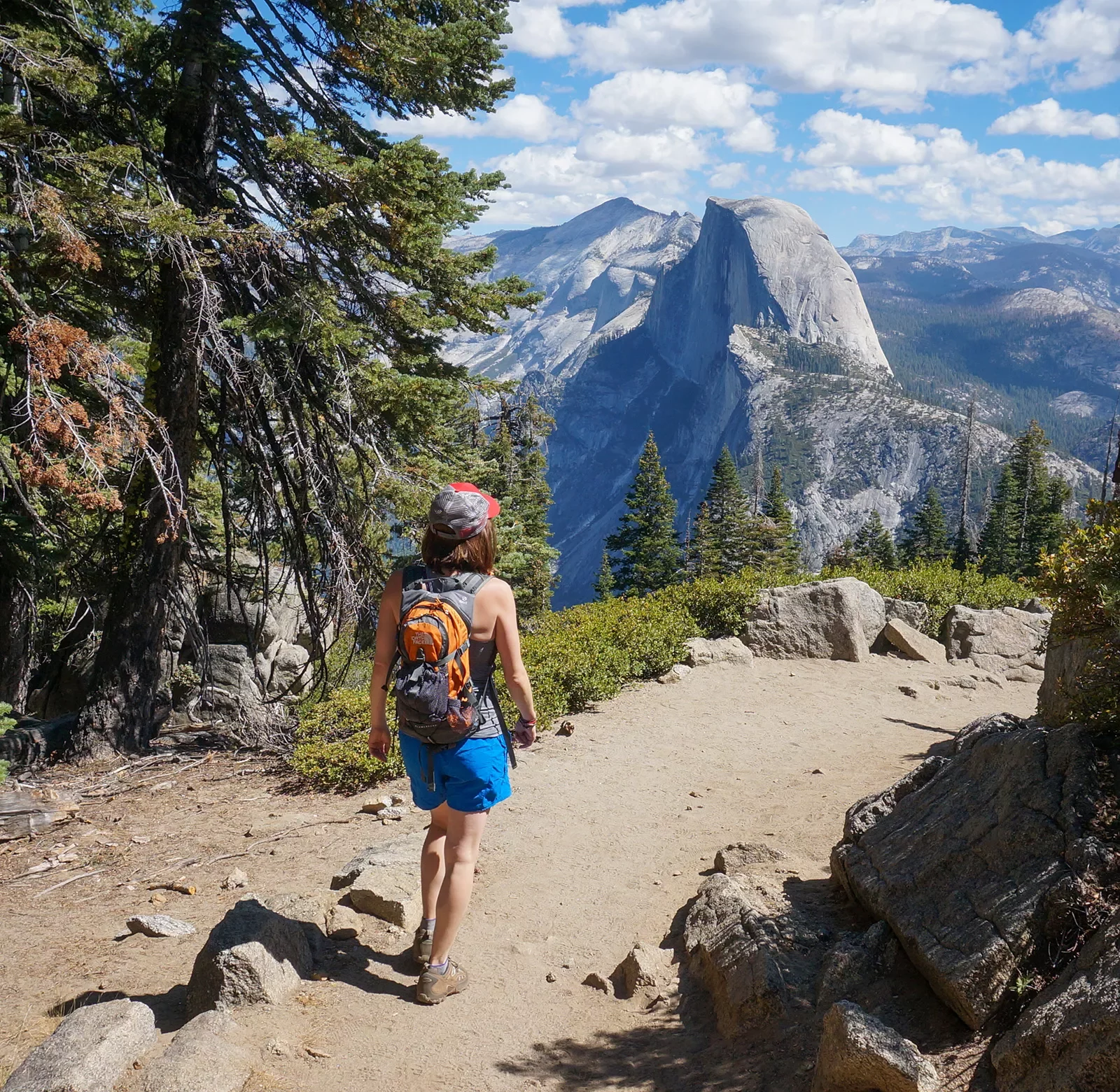 Guest walking on mountain trail, Half Dome in distance.