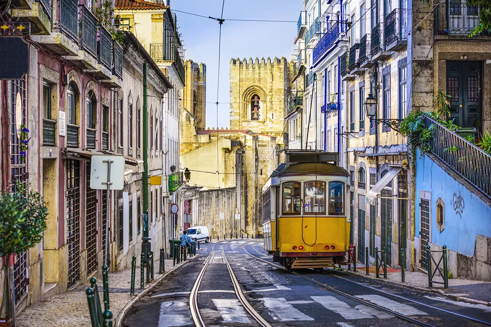 Street shot of Lisbon, Portugal. Tram, colorful buildings, stone tower in distance.
