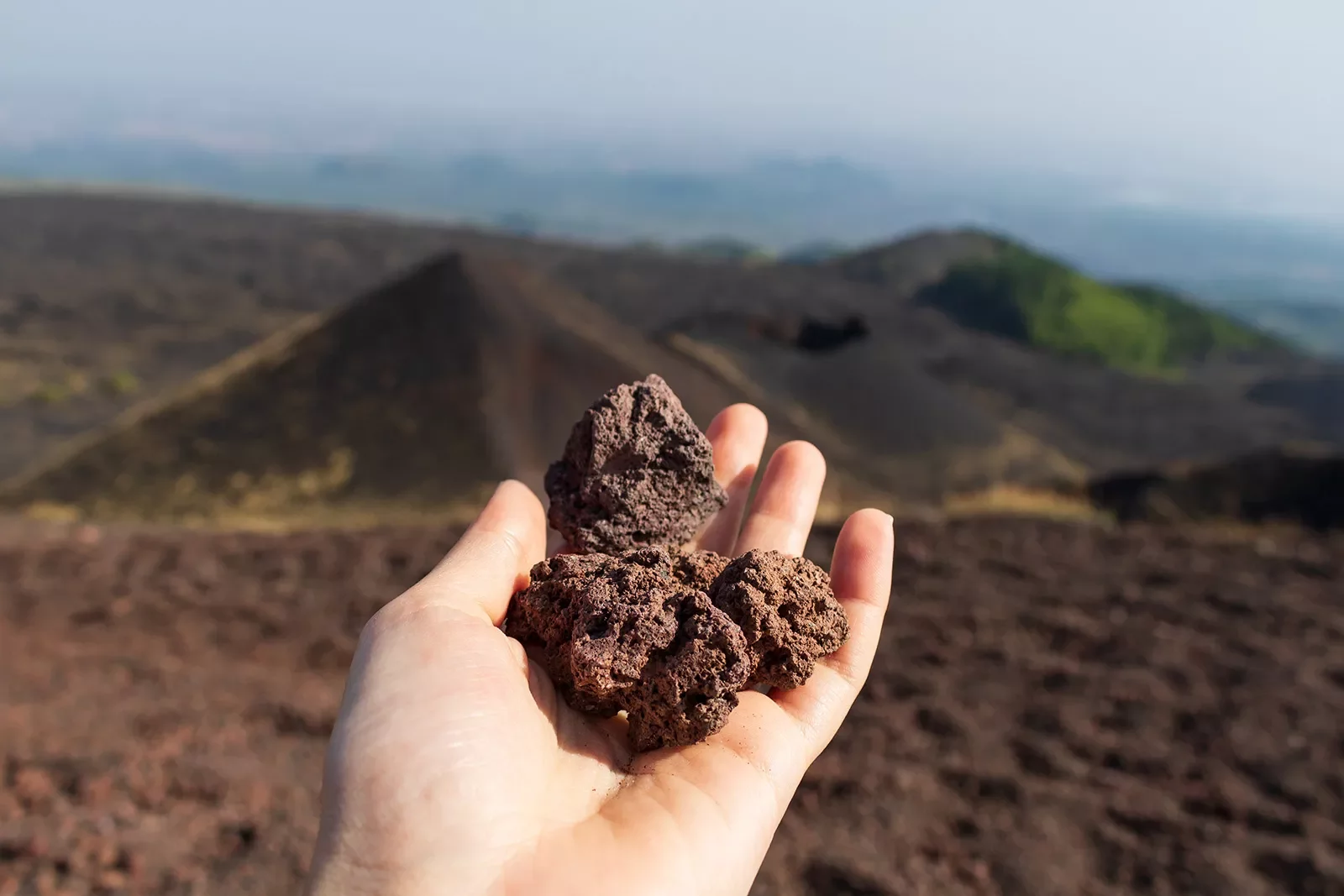 Point of view shot of volcanic rock landscape, hand holding volcanic rocks.