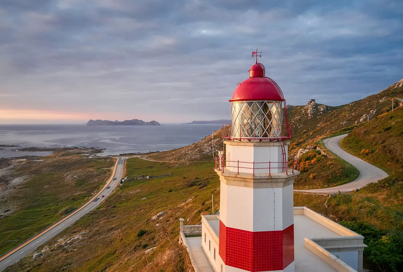 Wide shot of Spanish coastline during sunset, red and white lighthouse in foreground.