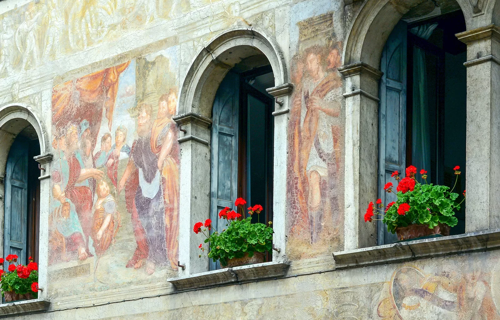 Shot of ancient mural on side of building, open windows, flowers.