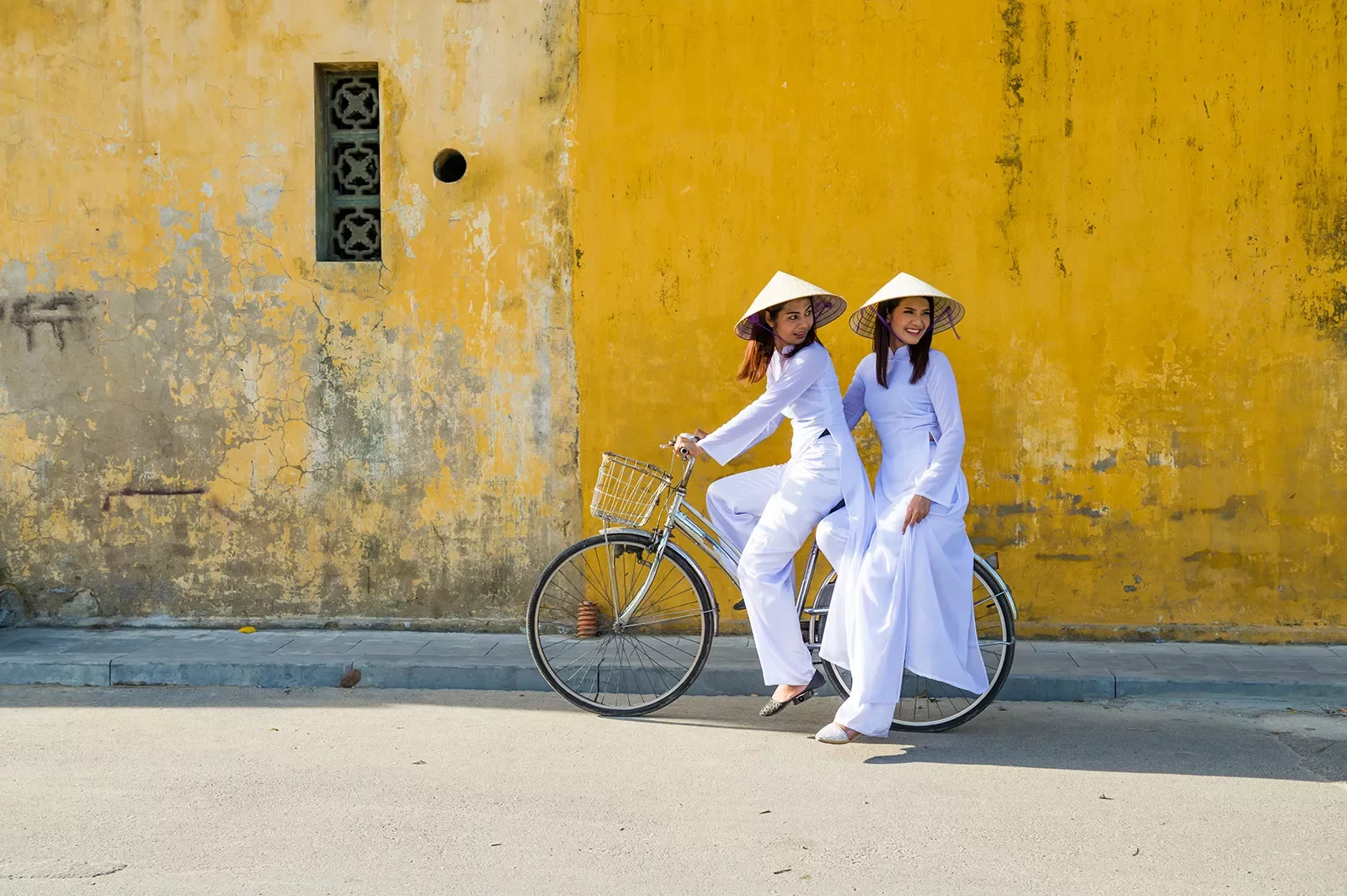 Two women on a bike in front of a yellow wall in Vietnam