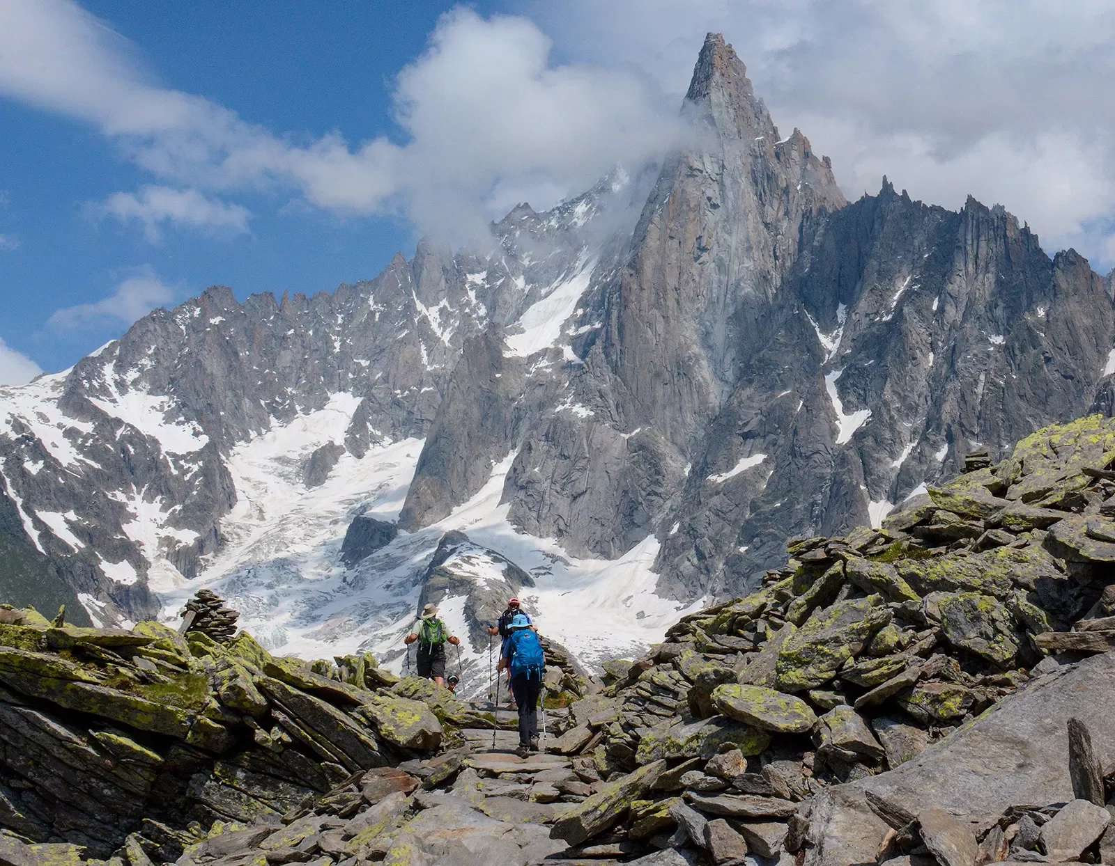 Two guests walking in craggy mountain pathway, large range in distance.