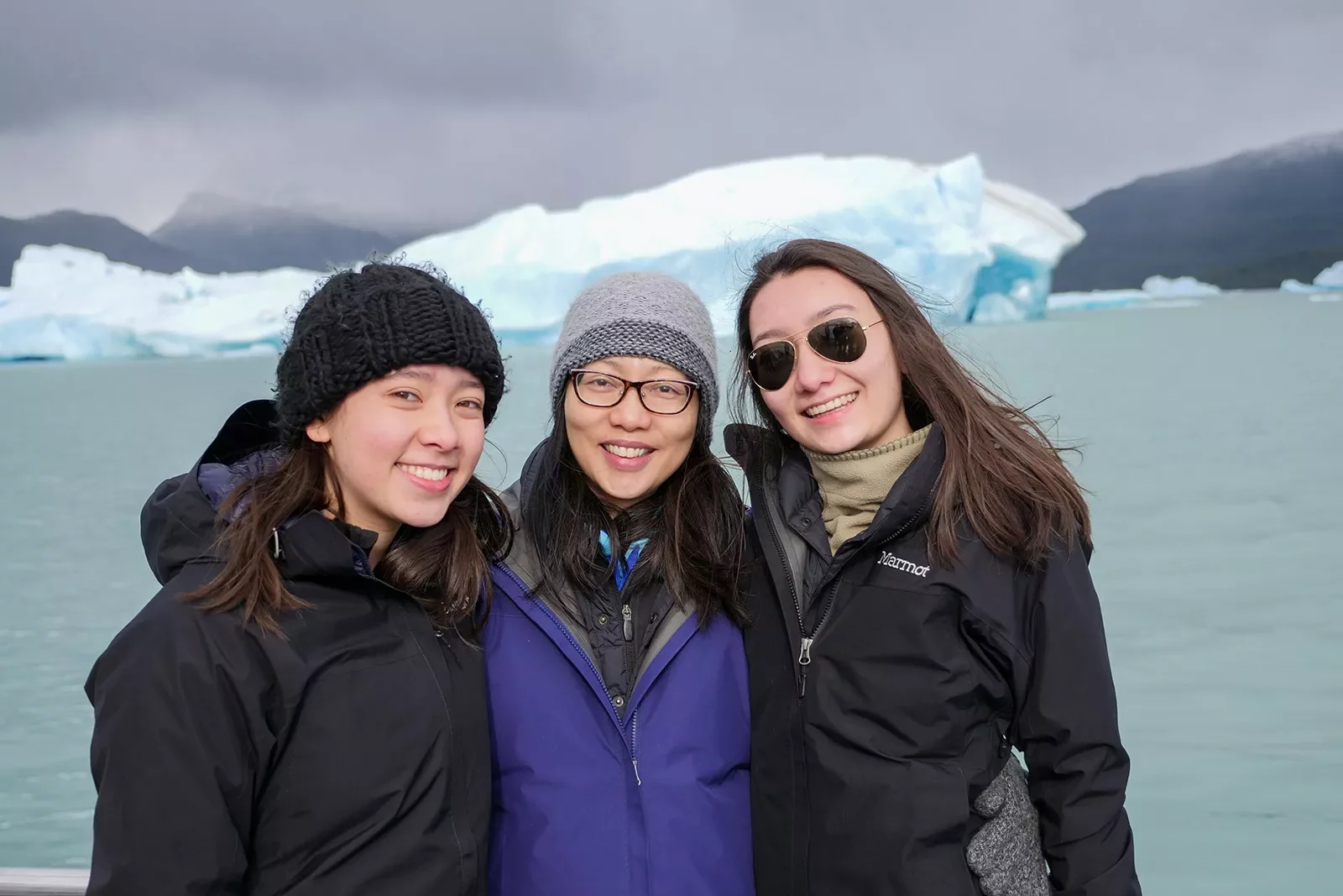 Three young guests smiling, large lake and glacier behind them.