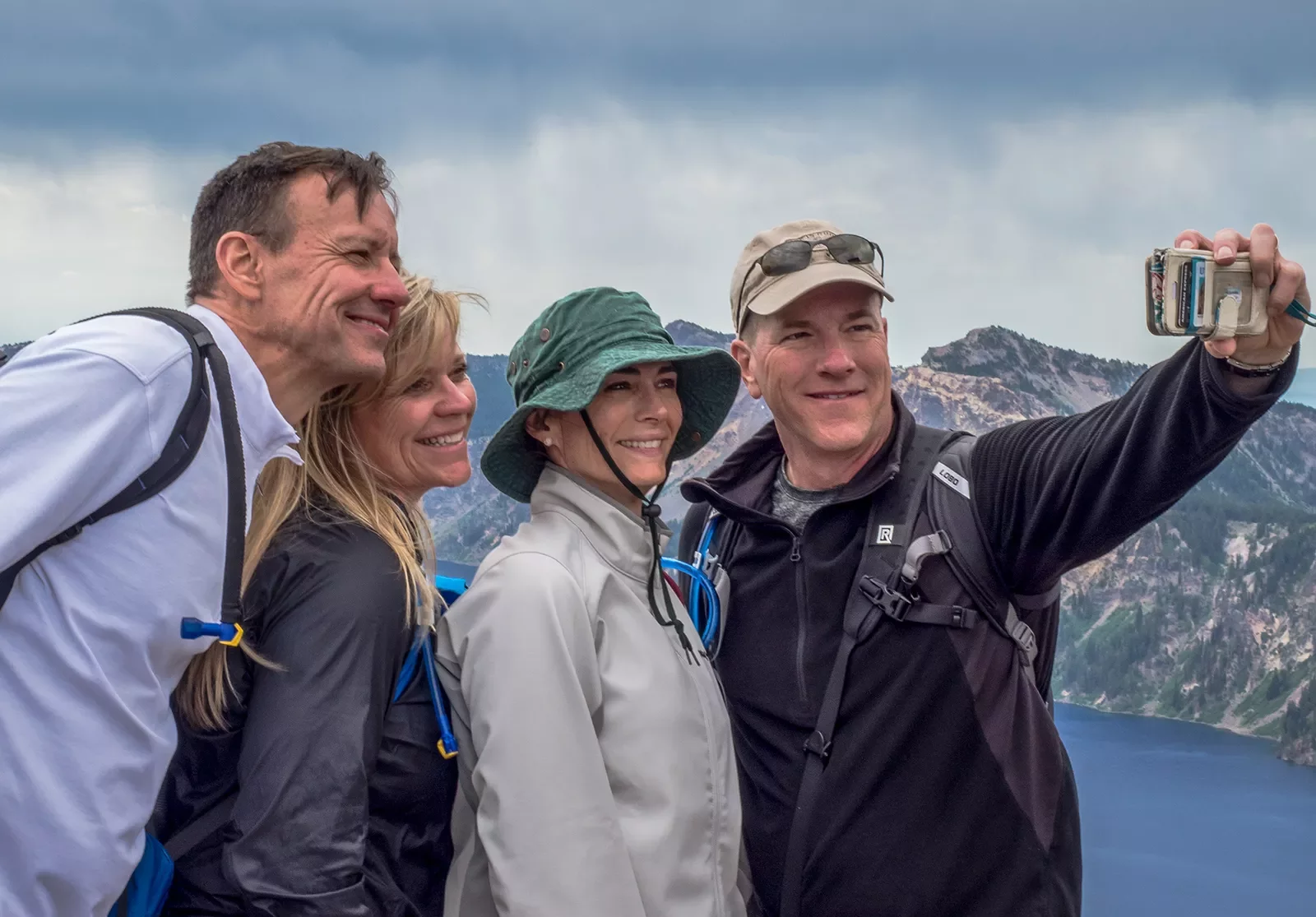 Four guests taking a selfie, lake and rocky cliffs in background.