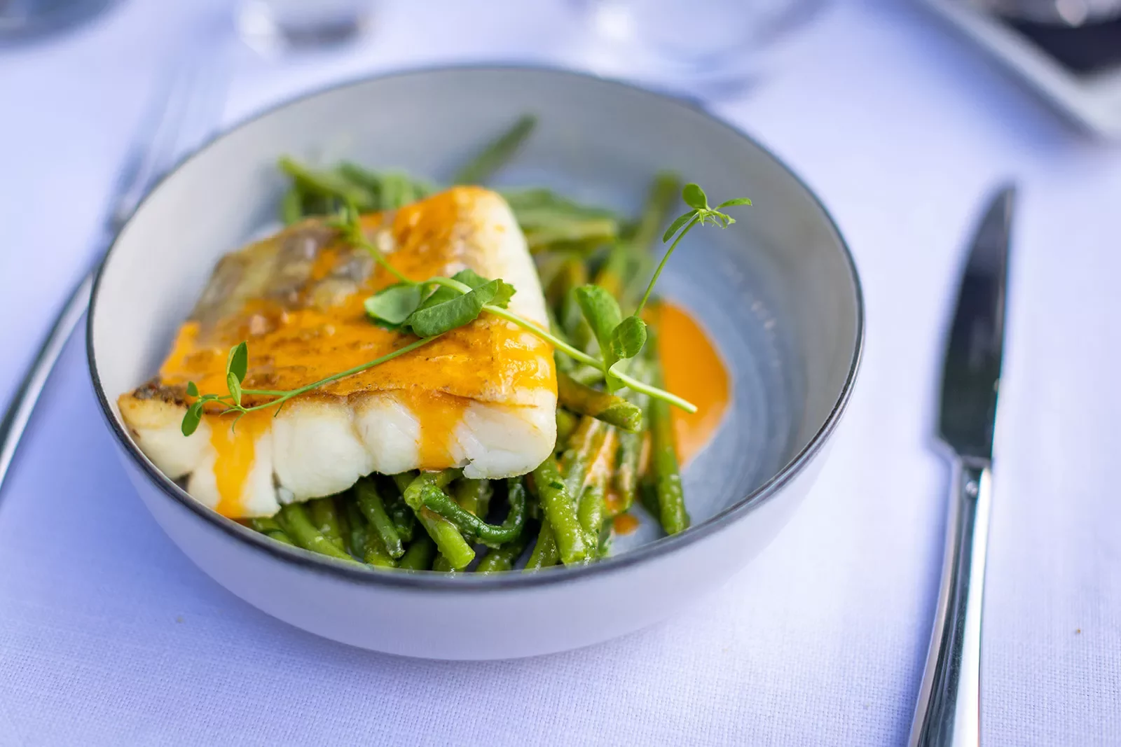 Plate of pan fried fish with an orange sauce, bed of greens.