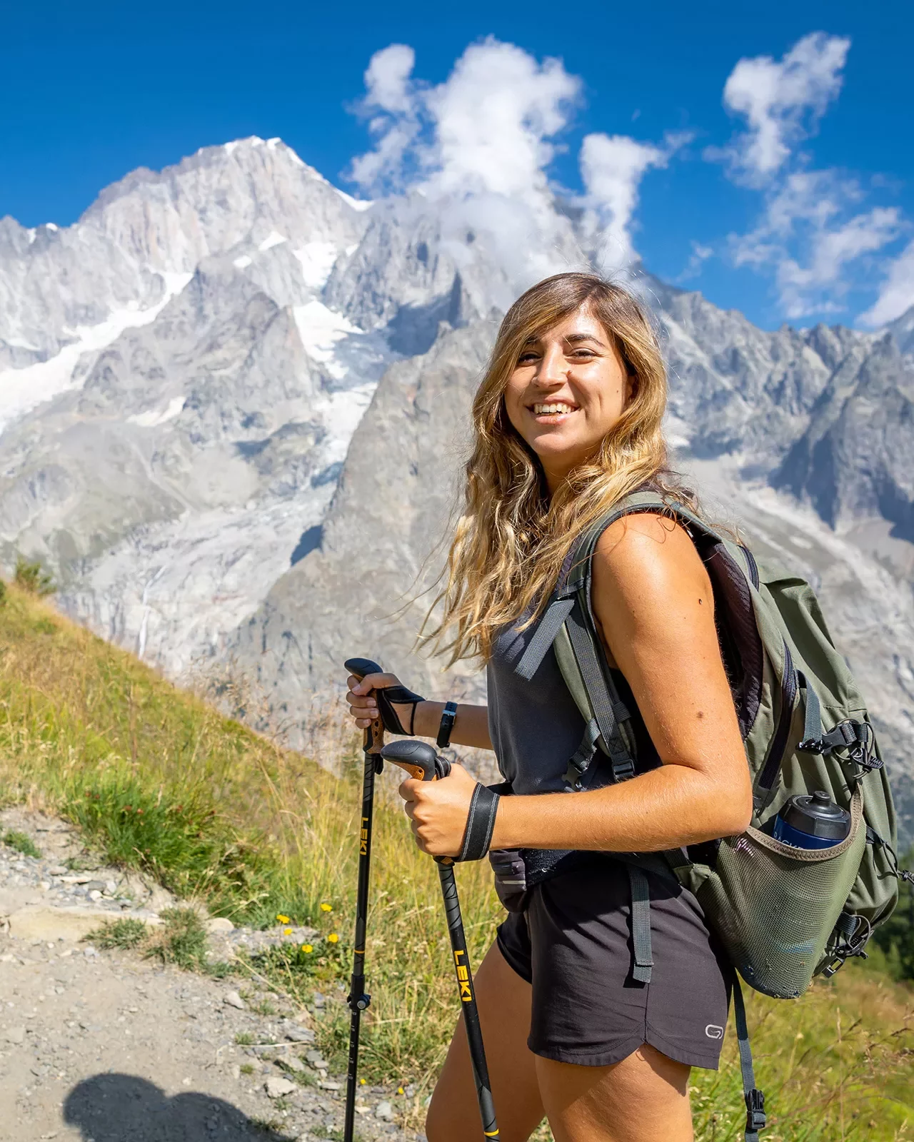 Guest with hiking poles smiling for camera, craggy mountains in distance.