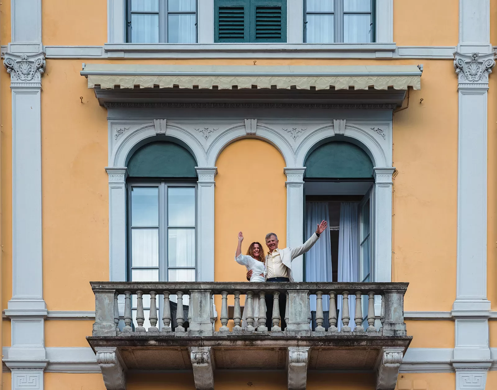 Two guests on balcony, waving to camera.