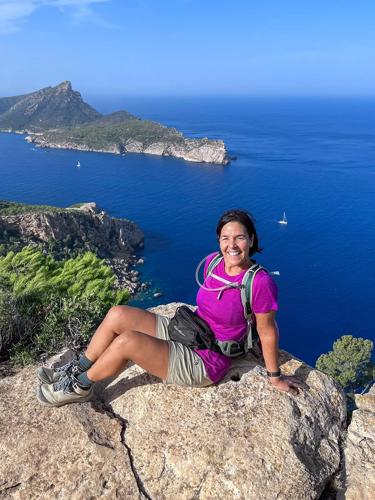 Guest posing on rock overlooking cliffside, ocean, island behind her.