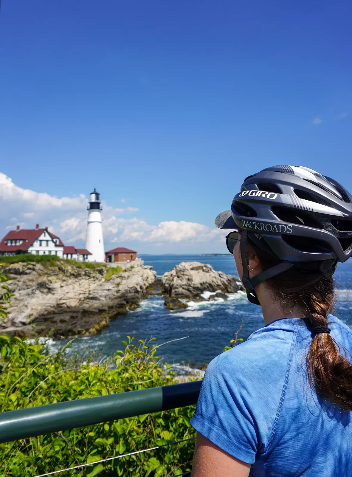 Caucasian woman in a bike helmet looks across a body of water at a lighthouse