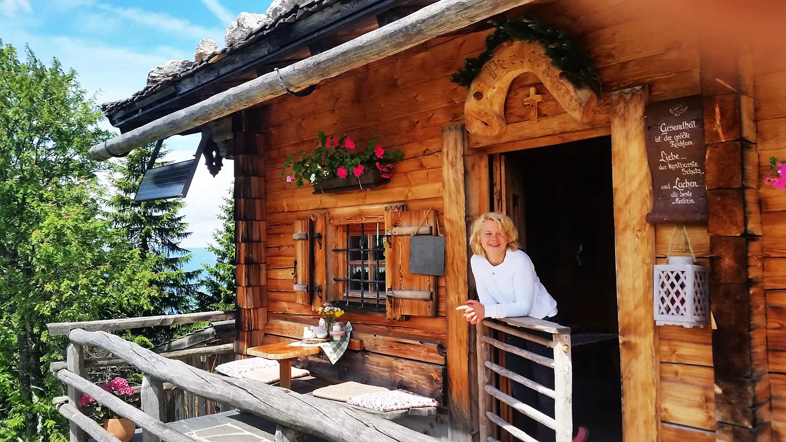 Woman leaning on balcony off of log cabin.