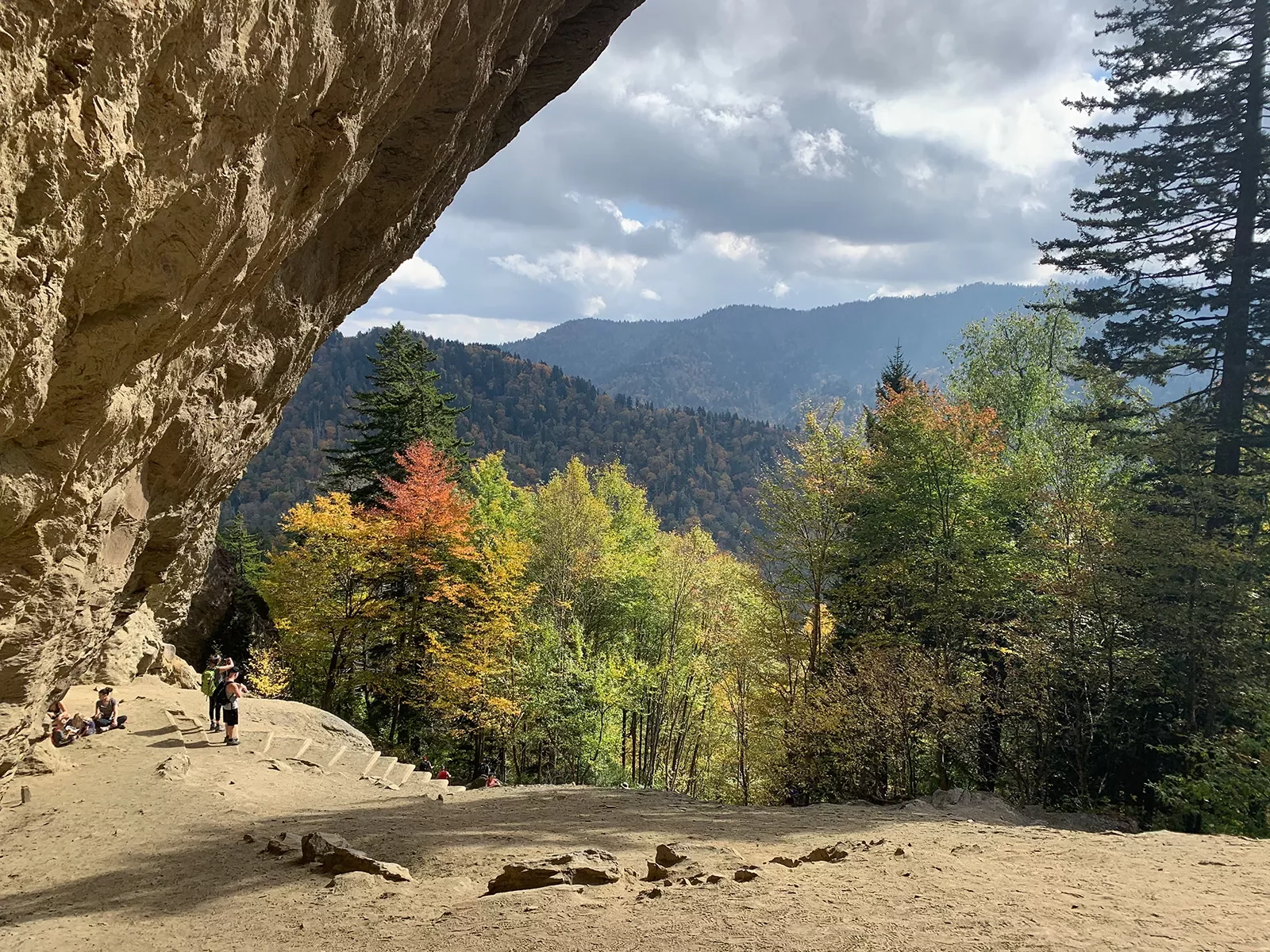 Guest walking under large cliff-face. Forest in background.
