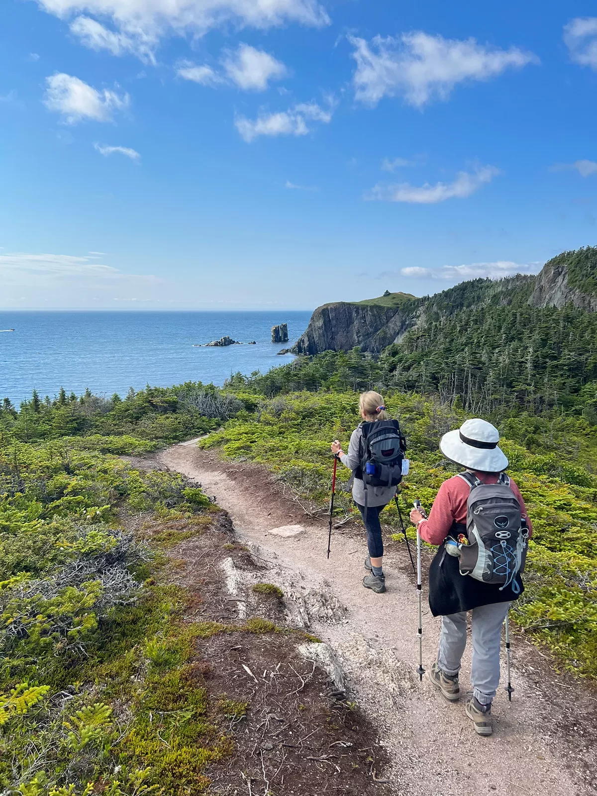 Two guests hiking towards ocean, rocky cliff to their right.